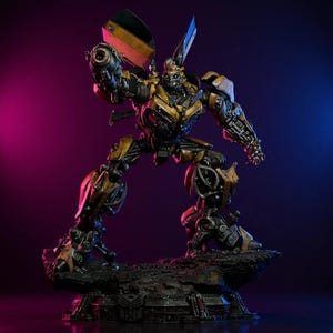 May include: A detailed statue of the Transformers character Bumblebee in a dynamic pose. The figure is primarily yellow and black, with intricate mechanical detailing. It stands on a rocky base with a metallic emblem, set against a gradient purple and blue background.