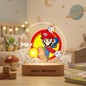 May include: A circular acrylic night light featuring a colorful graphic of Mario throwing a fireball, with the name MAX printed in white. The light is mounted on a rectangular wooden base engraved with the text HAPPY BIRTHDAY.