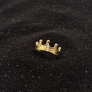 Peut inclure: Une bague couronne dorée avec un design détaillé. La bague est posée sur un fond sombre et texturé. La bague couronne est un bijou.