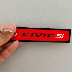 May include: A red and black keychain tag with the text "CIVIC Si" in white. The tag is rectangular and has a black border. A silver keyring is attached to the tag.