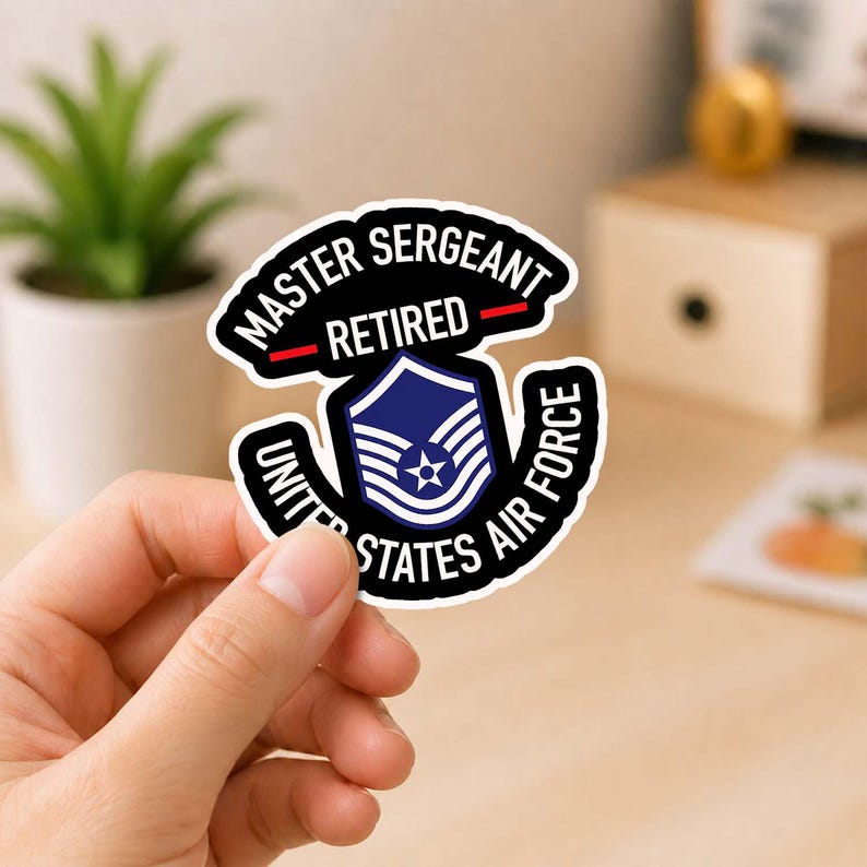 May include: A sticker featuring the text "MASTER SERGEANT RETIRED" above a blue and white Air Force emblem. The words "UNITED STATES AIR FORCE" are in a curved design around the emblem. The sticker is black and white.