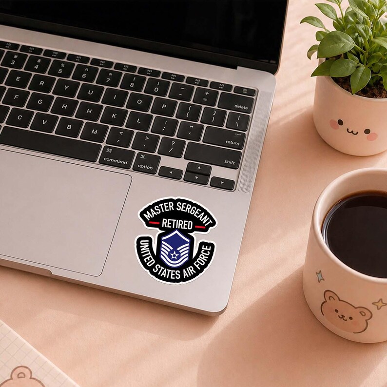 May include: A sticker on a laptop featuring the text "MASTER SERGEANT RETIRED UNITED STATES AIR FORCE" in a circular design. The sticker is black and white with a blue and white emblem in the center.