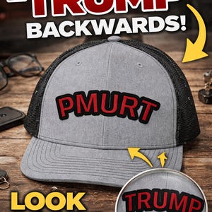 May include: A grey trucker cap with the word "PMURT" in red lettering. The text "IT SAYS 'TRUMP' BACKWARDS!" is above the cap. A magnifying glass shows the word "TRUMP". The text "LOOK AGAIN!" is below the cap.