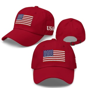 May include: A red baseball cap featuring an embroidered American flag on the front. The word "USA" is embroidered in white on the side. The cap has a curved brim and an adjustable strap.