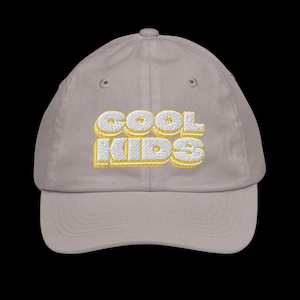 Puede incluir: Gorra de béisbol gris claro con el texto bordado "COOL KIDS" en blanco con un contorno amarillo. La gorra tiene una visera curva y un diseño de seis paneles.