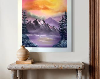 May include: Framed painting of a purple and pink mountain landscape with a yellow sunset in the sky. The painting is hanging on a white wall above a wooden table with two stools.