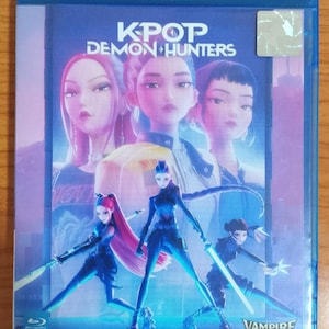 Puede incluir: Caja de disco Blu-ray de "KPOP Demon Hunters" con una vibrante ilustración de personajes animados. La portada presenta el texto del título y el logotipo de "Vampire House". La obra de arte muestra varias figuras femeninas con espadas.