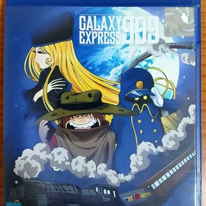 Puede incluir: Caja Blu-ray azul con la ilustración del anime "Galaxy Express 999". La portada muestra tres personajes, un tren y una luna sobre un fondo azul oscuro. También se ve el texto "Vampire House".