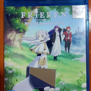 Puede incluir: Una taza de cerámica blanca con asa negra y el texto "But First, Coffee" en negrita negra. La taza se encuentra sobre un fondo borroso, sugiriendo un ambiente acogedor.
