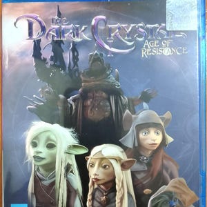 Puede incluir: Caja de disco Blu-ray azul de "El Cristal Oscuro: La Era de la Resistencia". La portada presenta personajes de la serie, con el título en una fuente estilizada. La caja tiene el logotipo de Blu-ray.