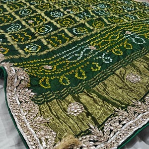 Puede incluir: Textil verde y dorado con dise&ntilde;os intrincados. La tela presenta un borde detallado con bordados florales y una borla decorativa. El dise&ntilde;o general es rico y ornamentado, con una mezcla de texturas y colores.