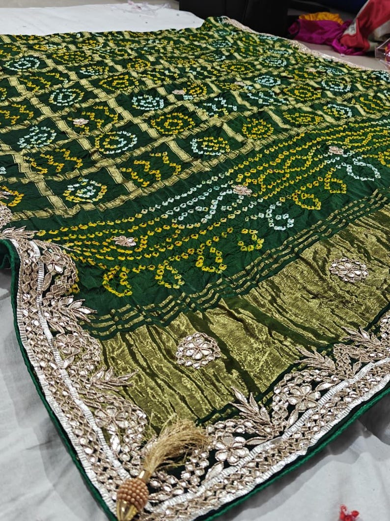 Puede incluir: Textil verde y dorado con dise&ntilde;os intrincados. La tela presenta un borde detallado con bordados florales y una borla decorativa. El dise&ntilde;o general es rico y ornamentado, con una mezcla de texturas y colores.