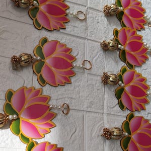 May include: Decorative garland featuring pink lotus flower cutouts with green and yellow accents. Each flower is connected by a string of pearls and gold-colored decorative elements. The garland is designed for festive or decorative purposes.