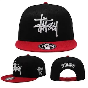 May include: Black and red baseball cap with the word "Stussy" in white script on the front. The cap has a flat brim and an adjustable strap. The Stussy logo is also on the back of the cap.