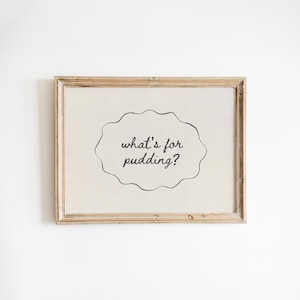 May include: A framed print with the text "what's for pudding?" in a whimsical font. The text is inside a free-form, cloud-like shape. The frame is a light brown color.