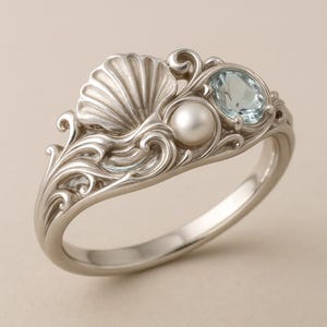 May include: A silver ring with a seashell design, featuring a pearl and a light blue oval gemstone. The ring has intricate wave and swirl details, creating a nautical theme. The ring is a size 7.