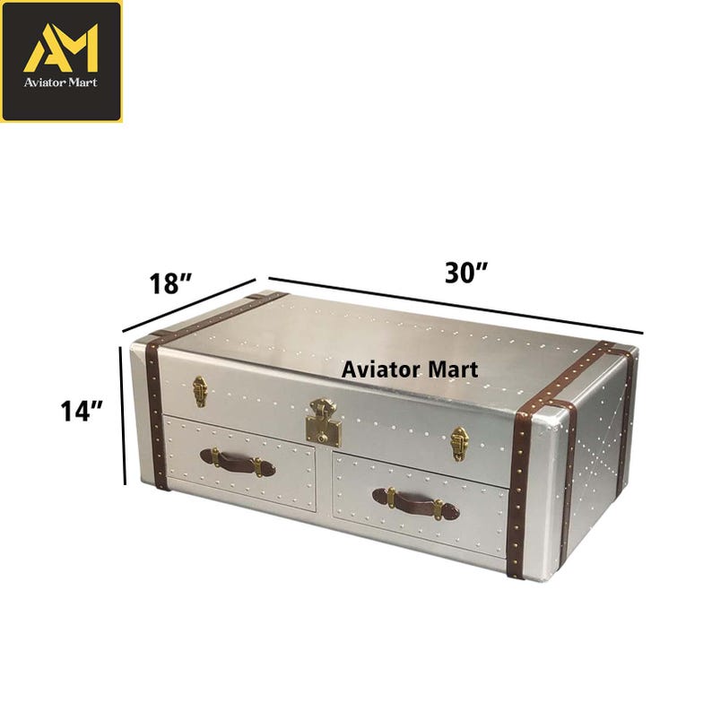 Puede incluir: Una mesa de centro plateada de metal con forma de ba&uacute;l, con ribetes de cuero marr&oacute;n y dos cajones. La mesa mide 76 cm de largo, 46 cm de ancho y 36 cm de alto. El texto "Aviator Mart" es visible.