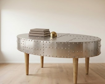 Mesa de centro redonda Aviator em alumínio rebitado, estilo industrial aeronáutico, para sala de estar, com pés modernos em madeira.