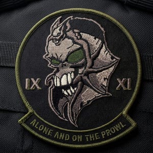 May include: Embroidered patch featuring a stylized skull with green eyes and sharp teeth. The patch is circular with a black background and a green border. The text "IX" and "XI" flank the skull, with "ALONE AND ON THE PROWL" below.