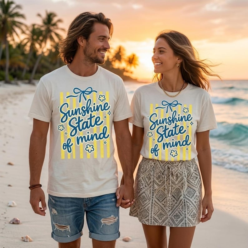 K&ouml;nnte beinhalten: Zwei Personen tragen passende cremefarbene T-Shirts mit dem Text "Sunshine State of Mind" in blauer Schrift und gelben Akzenten. Die Shirts haben eine Schleife und eine Blumen-Grafik. Sie halten sich am Strand an den H&auml;nden.