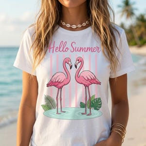 K&ouml;nnte beinhalten: Wei&szlig;es T-Shirt mit einem rosa Flamingo-Design und dem Text "Hello Summer". Die Grafik zeigt zwei rosa Flamingos, rosa und wei&szlig;e Streifen und tropische Bl&auml;tter. Ein Sommer-Themen-Kleidungsst&uuml;ck.