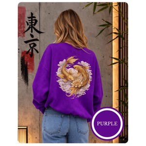 Puede incluir: Una sudadera morada con un diseño de peces koi dorados en la espalda. El diseño incluye dos peces koi, una flor de loto y detalles de nubes. La palabra "Tokyo" está escrita en caracteres japoneses negros en el lado izquierdo.