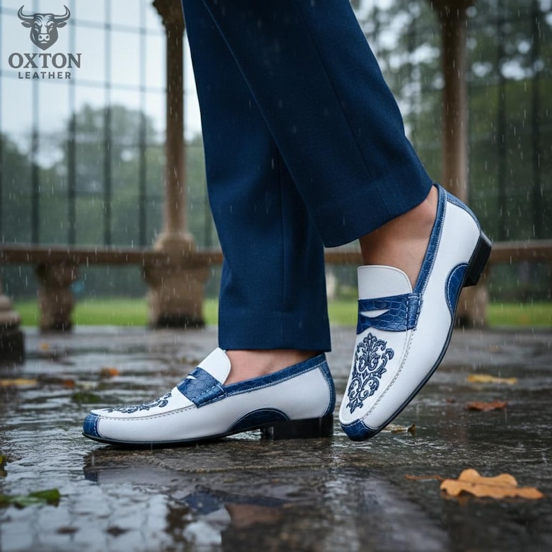 May include: White and blue leather loafers with an ornate design on the vamp. The shoes have a blue trim and a textured blue accent on the tongue. The Oxton Leather logo is visible in the background.