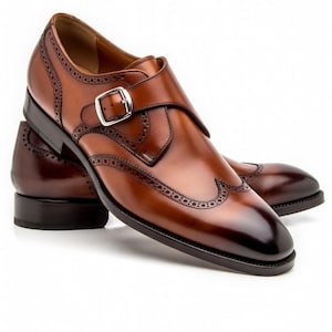 May include: A pair of brown leather dress shoes with a single monk strap buckle. The shoes feature a wingtip design with decorative perforations and a polished finish. The soles are dark brown.