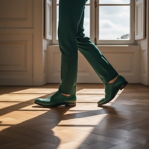 May include: Green leather dress shoes with a classic lace-up design. The shoes are paired with matching green trousers. The image is taken indoors with natural light, highlighting the texture and color of the shoes.