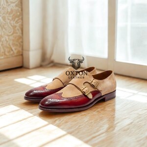 May include: Two-tone leather dress shoes with a burgundy toe and tan suede upper. The shoes have a double monk strap closure with gold-coloured buckles. The "OXTON LEATHER" logo is visible.