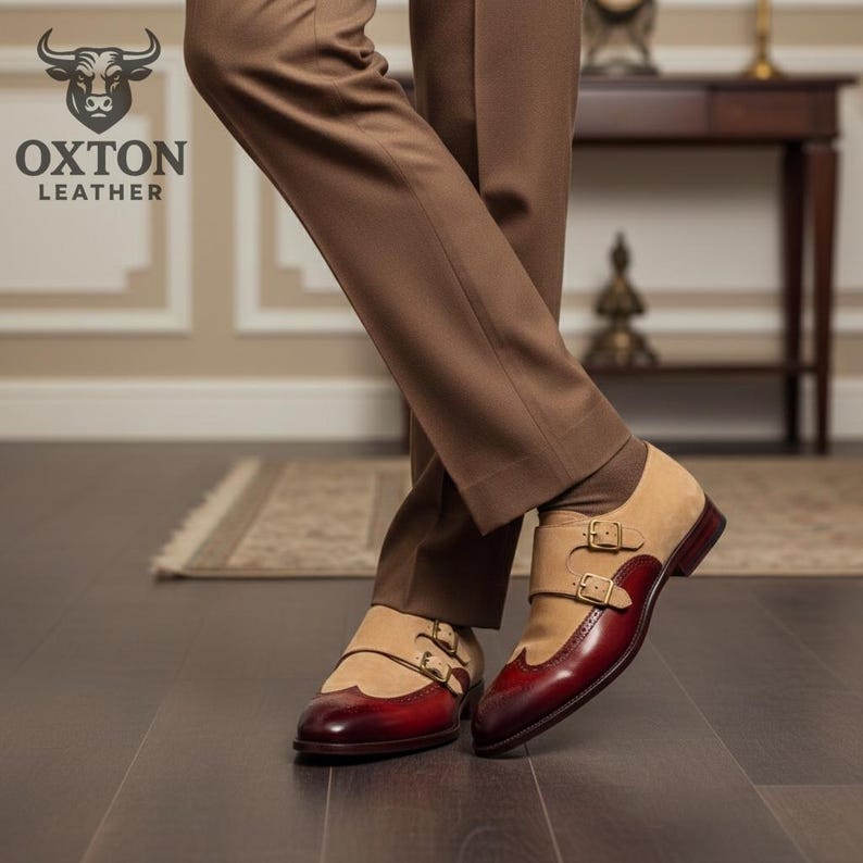 May include: Tan and burgundy leather double-buckle shoes. The shoes feature a suede upper and a burgundy leather toe cap and heel. The shoes are worn with brown trousers. The Oxton Leather logo is visible in the upper left corner.