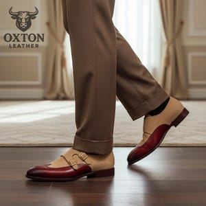 May include: Two-tone leather dress shoes with a burgundy toe and heel, and a tan upper. The shoes feature a double monk strap closure with gold-coloured buckles. The brand logo "OXTON LEATHER" is visible in the upper left corner.