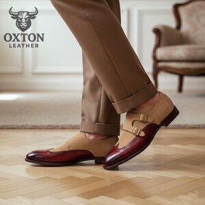 May include: Tan and burgundy leather double monk strap shoes with a wingtip design. The shoes feature a suede upper and polished leather toe and heel. Gold-coloured buckles secure the straps. The Oxton Leather logo is visible in the upper left corner.