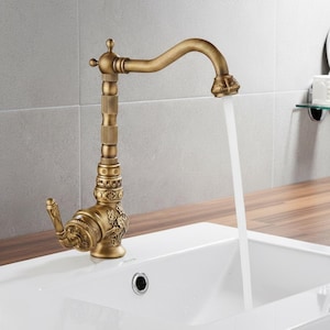 Può includere: Un rubinetto in ottone in stile antico con intricati dettagli floreali e a volute. Il rubinetto ha un beccuccio curvo e una maniglia a leva. L'acqua scorre dal beccuccio in un lavandino bianco. Un elemento decorativo per bagno o cucina.