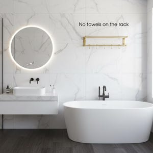 May include: A modern bathroom with a white bathtub, sink, and a round mirror with a glowing light. The walls are white with marble-like veining. A gold towel rack is mounted on the wall. Text on the wall reads: "No towels on the rack."