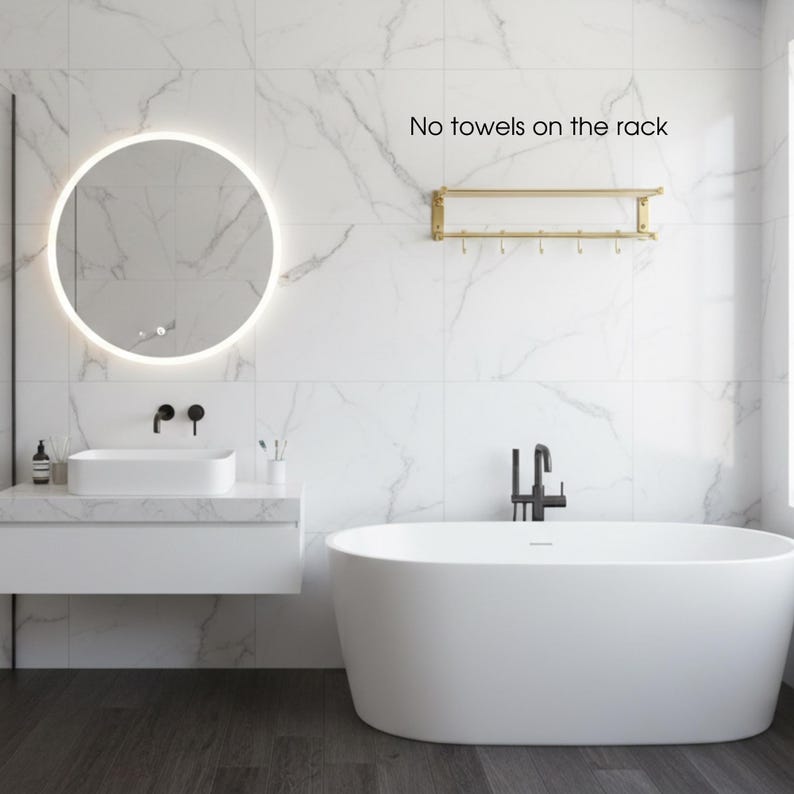 May include: A modern bathroom with a white bathtub, sink, and a round mirror with a glowing light. The walls are white with marble-like veining. A gold towel rack is mounted on the wall. Text on the wall reads: "No towels on the rack."