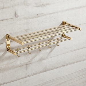 May include: A gold-colored metal bathroom shelf with a towel rack and hooks. The shelf has a rectangular shape with multiple horizontal bars for towels. Below, there is a bar with several hooks for hanging items. The fixture is mounted on a light-colored wooden wall.