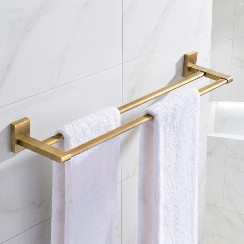 Peut inclure: Un porte-serviettes double en laiton bross&eacute;, mont&eacute; sur un mur carrel&eacute; blanc. Deux serviettes blanches sont suspendues &agrave; la barre. Les plaques de montage et la barre rectangulaires ont un design simple et moderne.