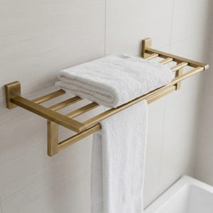 Op de afbeelding: Een goudkleurige metalen handdoekenrek aan een witte betegelde muur. Het rek bevat een opgevouwen witte handdoek bovenop en een hangende witte handdoek eronder. Het rek heeft een rechthoekig ontwerp.
