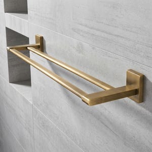 Peut inclure: Un porte-serviettes double en laiton, mont&eacute; sur un mur carrel&eacute; gris clair. Le porte-serviettes a une base rectangulaire et deux barres parall&egrave;les pour suspendre les serviettes. La finition en laiton lui donne un aspect classique et &eacute;l&eacute;gant.