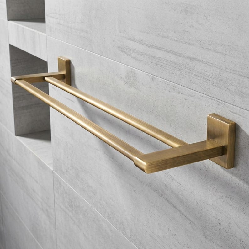 Peut inclure: Un porte-serviettes double en laiton, mont&eacute; sur un mur carrel&eacute; gris clair. Le porte-serviettes a une base rectangulaire et deux barres parall&egrave;les pour suspendre les serviettes. La finition en laiton lui donne un aspect classique et &eacute;l&eacute;gant.