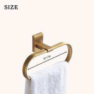 Peut inclure: Un porte-serviettes dor&eacute; avec une serviette blanche. Le cercle mesure 20 cm de large et est mont&eacute; sur une base carr&eacute;e. Le mot "SIZE" est dans le coin sup&eacute;rieur gauche.