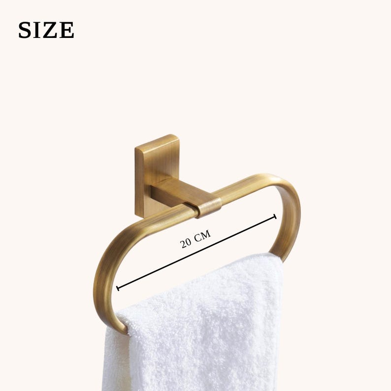 Peut inclure: Un porte-serviettes dor&eacute; avec une serviette blanche. Le cercle mesure 20 cm de large et est mont&eacute; sur une base carr&eacute;e. Le mot "SIZE" est dans le coin sup&eacute;rieur gauche.