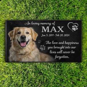 May include: A black rectangular pet memorial stone with a photo of a golden retriever dog named Max. The text reads "In loving memory of MAX" with dates and a heartfelt message about love and happiness.