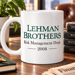 May include: A white ceramic mug featuring the dark green text LEHMAN BROTHERS, followed by the black text Risk Management Dept. and the year 2008 centred below. The mug has a curved handle on the left side and a smooth, glossy finish.