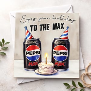 May include: Birthday card with two Pepsi Max cans wearing party hats, a small cake with a lit candle. The card reads "Enjoy your birthday TO THE MAX". The Pepsi cans have red, white, and blue logos. The cake is on a small plate.