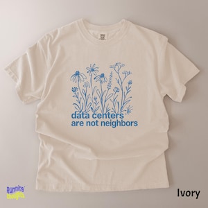 May include: An ivory short-sleeve t-shirt featuring a blue line-art graphic of various wildflowers. Below the floral illustration, the text reads, "data centers are not neighbors" in a simple, lowercase, blue sans-serif font.
