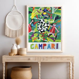 May include: A framed rectangular art print featuring a stylized soccer match scene with geometric shapes in green, red, blue, and yellow. The word CAMPARI is printed in large, colorful block letters at the bottom of the composition.