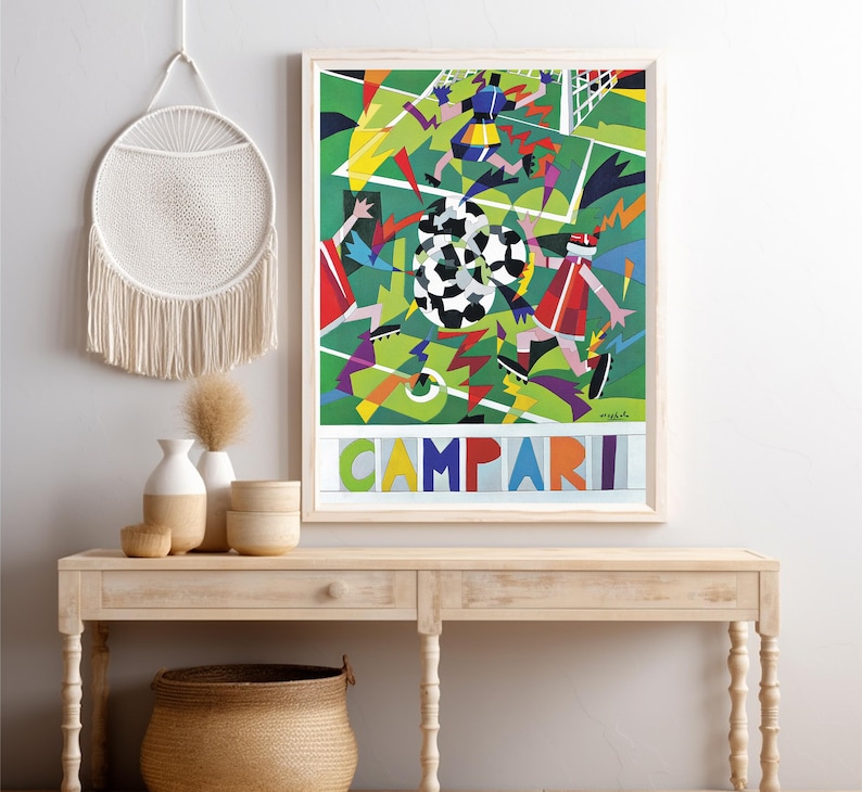 May include: A framed rectangular art print featuring a stylized soccer match scene with geometric shapes in green, red, blue, and yellow. The word CAMPARI is printed in large, colorful block letters at the bottom of the composition.