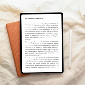 May include: A black tablet displaying text titled "How to Structure a Strong Answer" with a white stylus and an orange notebook. The tablet's screen shows paragraphs of text. The notebook is open, revealing its orange pages.